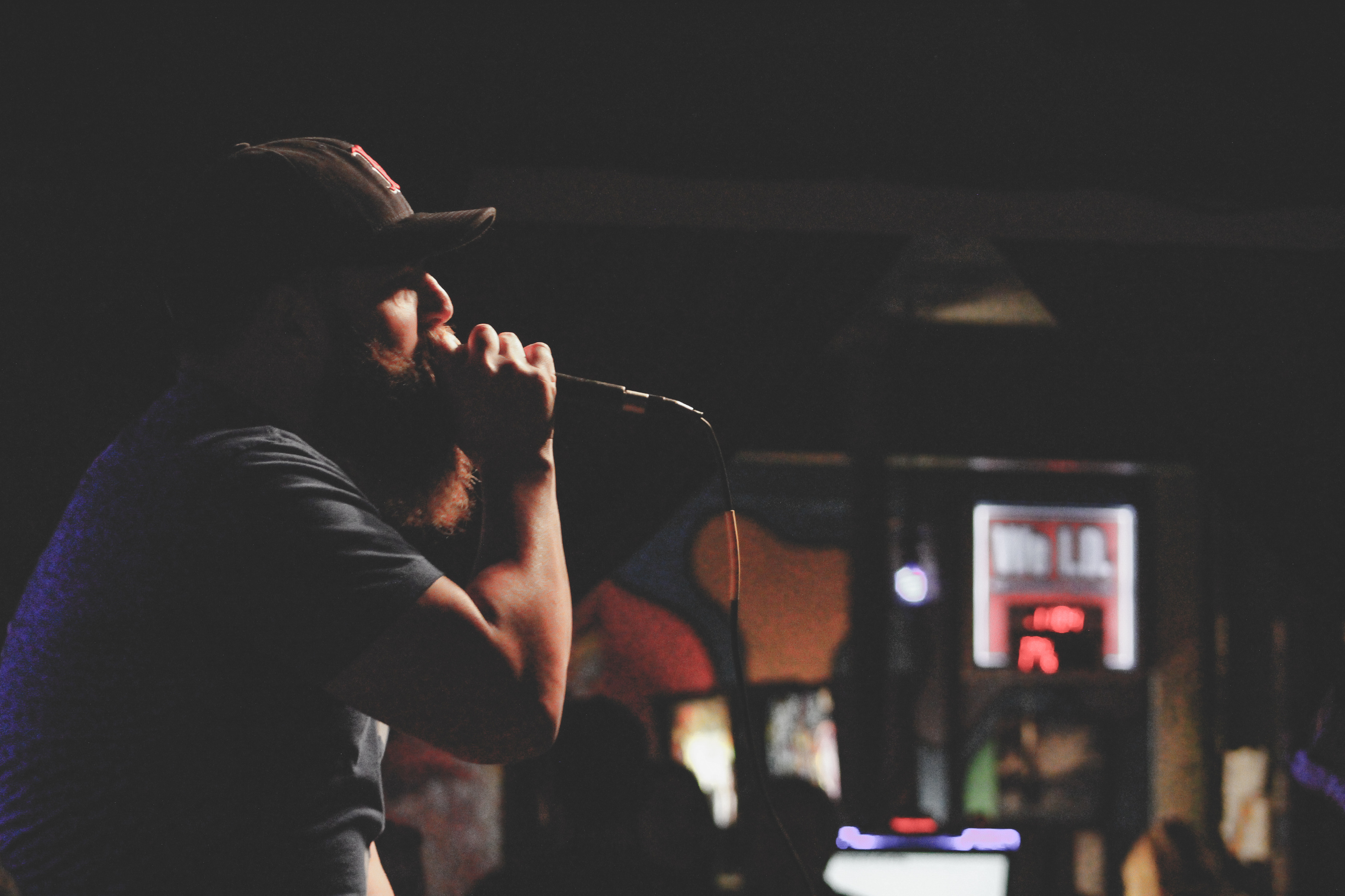 Man Wearing Grey Shirt and Black Cap Singing Using Corded Microphone